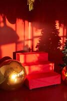 A red ladder on a red background. The shadow of a Christmas tree on the wall. The room's New Year's decor is decorated in red tones. With space to copy photo