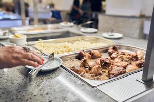 A healthy buffet in a restaurant or at an event. Delicious dishes for a late dinner on plates. A hand holds a pair of tongs for applying chicken photo