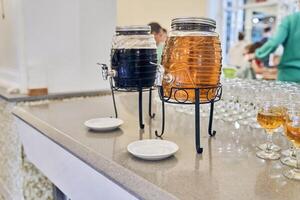 Juice from fresh fruits in the vending machine. Drinks are served on the table in a glass barrel with a tap. Drinks for catering at a party. photo