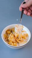A close-up shot of a spoon lifting a portion of golden cornflakes soaked in fresh milk from a bowl, Vertical video