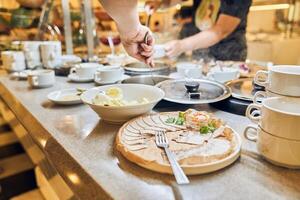 A person selects and serves breakfast dishes in the hotel restaurant. Buffet for a hearty lunch with space for copying photo