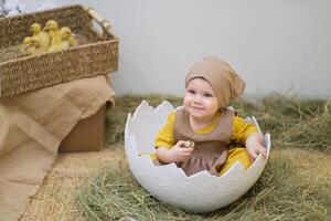 A baby in a brown outfit sitting in an egg photo
