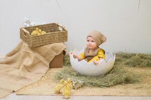 A baby sitting in an egg shell with a basket of ducks photo