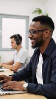 A smiley biracial man in glasses and headset takes notes while attending a webinar on his laptop photo
