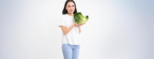 Portrait of lovely korean woman, showing cabbage, holding lettuce green vegetable and smiling, isolated on white background photo