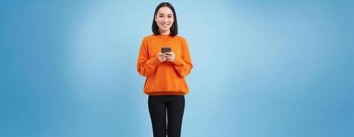 Girl with smartphone in hands smiling, using mobile application on her phone, sending message or order something online, blue background photo