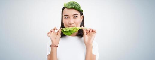 Portrait of asian girl with leaf on head, eats cabbage and smiles, isolated on white background photo