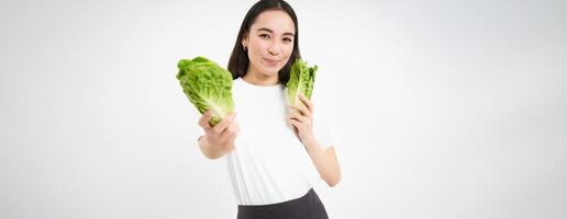 Smiling asian woman, vegan eating cabbage, enjoys tasty fresh lettuce leaves, stands over white background photo