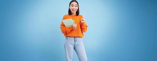Smiling asian woman with notebooks, student with happy face, promo of college education, blue background photo