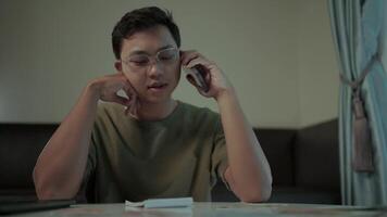 Focused on the call. A young man in casual attire sits at a table, engrossed in a phone call, showcasing a moment of focused communication and quiet contemplation. video