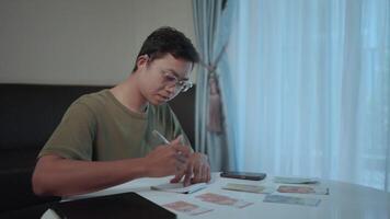 Focused on finances. a young man meticulously manages his budget, carefully calculating expenses while seated at a table, showcasing the importance of financial planning. video