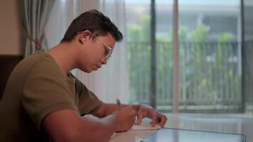 Focused on the task a young man concentrates intently on writing in his journal, his expression focused and determined, as he seeks clarity and introspection in the comfort of his home. video