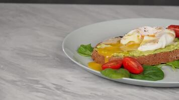 Delicious avocado toast with poached egg and cherry tomatoes on marble table video