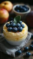 Creamy dessert topped with fresh blueberries served in a bowl on a wooden table surrounded by fruits photo