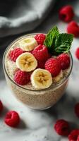 Healthy chia pudding topped with sliced banana and fresh raspberries in a clear glass bowl photo