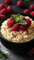 Creamy rice pudding topped with fresh raspberries and mint leaves in a black bowl photo