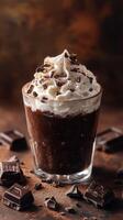 Rich chocolate dessert topped with whipped cream and chocolate shavings served in a glass with chocolate pieces on the side photo