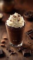 Rich chocolate dessert topped with whipped cream and shaved chocolate in a glass on a wooden table photo