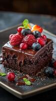 Decadent chocolate cake topped with fresh berries served on a black plate photo