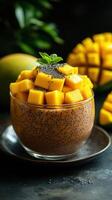 Fresh mango chia pudding served in a glass bowl with mint leaf decoration on a dark table photo