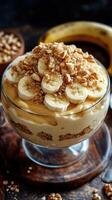 Delicious layered banana dessert with crushed nuts and creamy filling topped with ripe banana slices in a clear glass dish photo