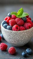 Freshly picked raspberries and blueberries in a speckled bowl with mint leaves on a dark background photo