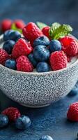 Fresh berries in a decorative bowl placed on a blue textured surface with scattered fruits nearby photo