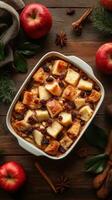 Delicious apple bread pudding with spices and raisins served in a white dish on a wooden table photo