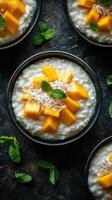 Delicious mango coconut rice pudding served in black bowls with fresh mint leaves photo