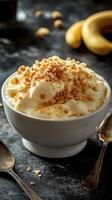 Banana pudding topped with crushed cookies and served in a white bowl on a dark textured surface photo