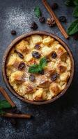 Delicious bread pudding topped with raisins and mint leaves served in a brown bowl on a dark surface photo