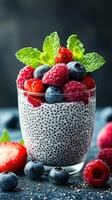 Chia seed pudding topped with fresh berries and mint leaves served in a clear glass against a dark background photo