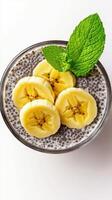 Chia seed pudding topped with fresh banana slices and mint leaves in a glass bowl on a white background photo