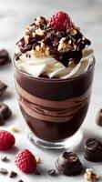 Indulgent chocolate dessert with whipped cream, raspberries, and crunch topping served in a clear glass on marble surface photo