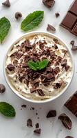 Delicious dessert bowl with whipped cream, chocolate shavings, and mint leaves on a white table photo