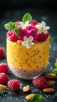Delicious mango chia pudding topped with fresh raspberries and edible flowers on a dark surface photo