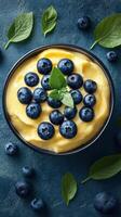 Delicious bowl of creamy dessert topped with fresh blueberries and mint leaves on a textured blue background photo