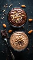 Delicious chocolate and vanilla dessert cups topped with crushed nuts served on a dark stone surface photo