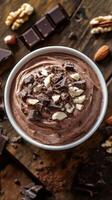 Creamy chocolate mousse topped with chopped nuts and dark chocolate pieces resting on a rustic wooden table photo