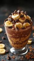 Delicious chocolate dessert with banana and chocolate chunks served in a glass bowl on a dark countertop photo