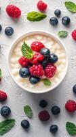 Creamy dessert bowl topped with fresh raspberries, blueberries, and mint leaves on a textured surface photo