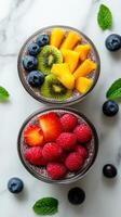 Colorful fruit bowls with chia pudding displayed on a marble countertop surrounded by fresh blueberries and mint leaves photo
