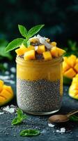 Delicious mango chia pudding topped with fresh mango and mint leaves in a jar on a dark background photo