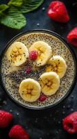 Chia seed pudding topped with banana and raspberries in a vibrant bowl on a dark background photo