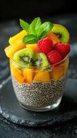 Colorful tropical dessert with chia seeds, fresh fruits, and mint leaves in a glass bowl on a dark surface photo