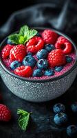 Fresh berries in a textured bowl with mint on a dark background showcasing a vibrant dessert photo