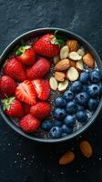 Berry and nut breakfast bowl featuring fresh strawberries and blueberries with chia seeds, served in a black bowl on a dark textured surface photo