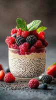 Delicious chia pudding topped with fresh berries and mint leaves served in a glass on a textured surface photo