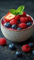 Colorful bowl of mixed berries with chia seeds and mint on a dark textured surface photo