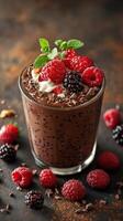 Decadent chocolate dessert in a glass topped with fresh berries and mint leaves served on a rustic wooden table photo